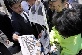 Japonci s novinami oznamujícími rezignaci premiéra.